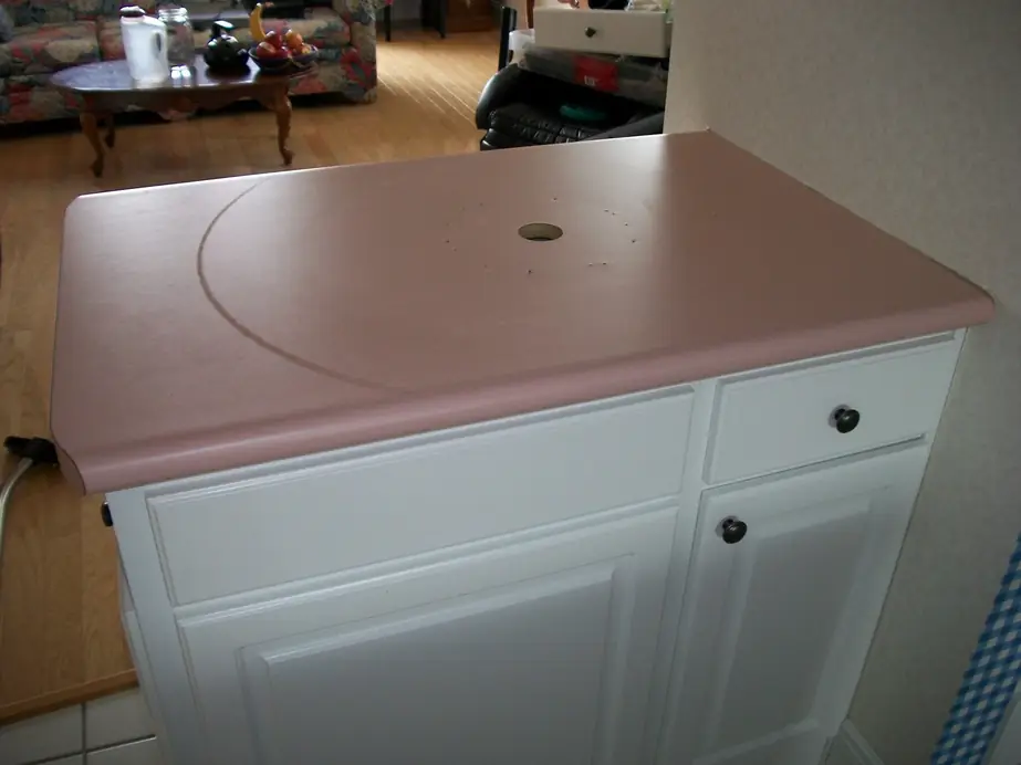 Pink laminate kitchen counter on a white cabinet before refinishing